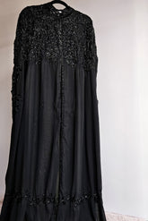 Black dress with bead embellishments on a hanger against a plain background